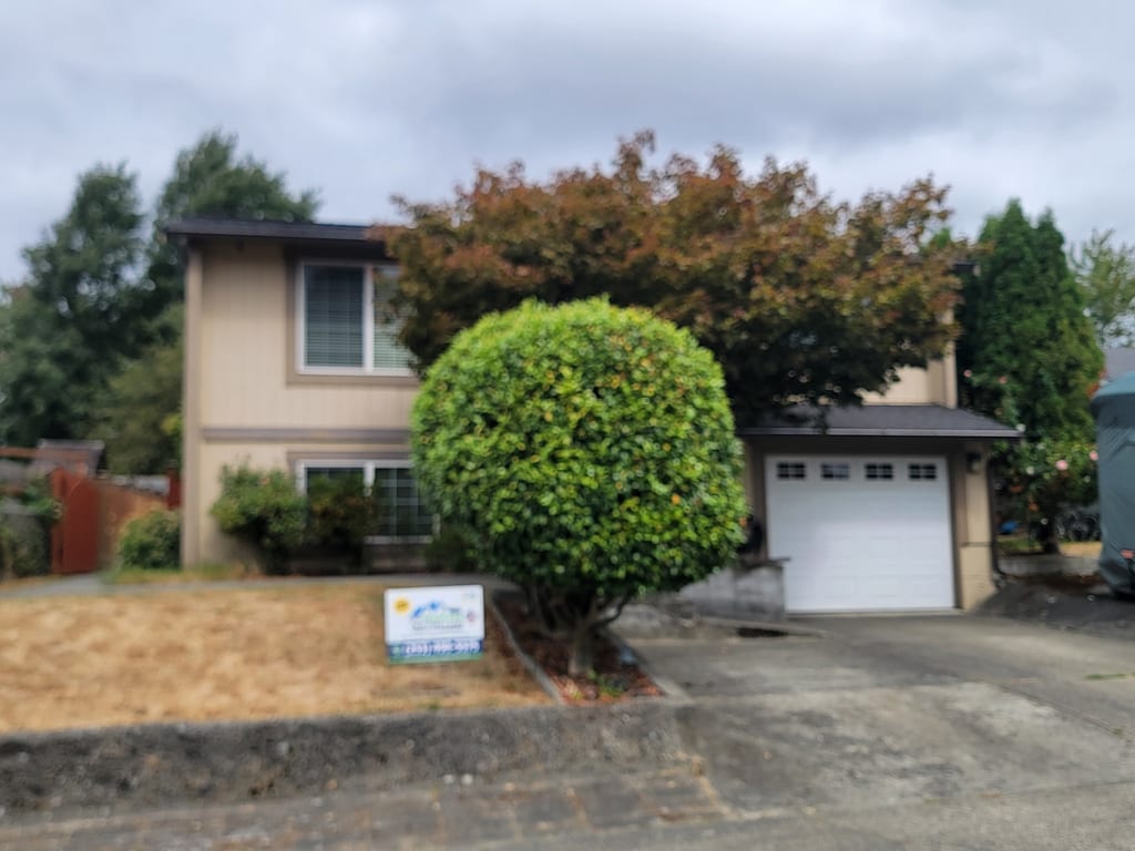 Two-story split-level home with new dark seamless gutters and a Seamless Gutters 4 Less yard sign in the front yard.